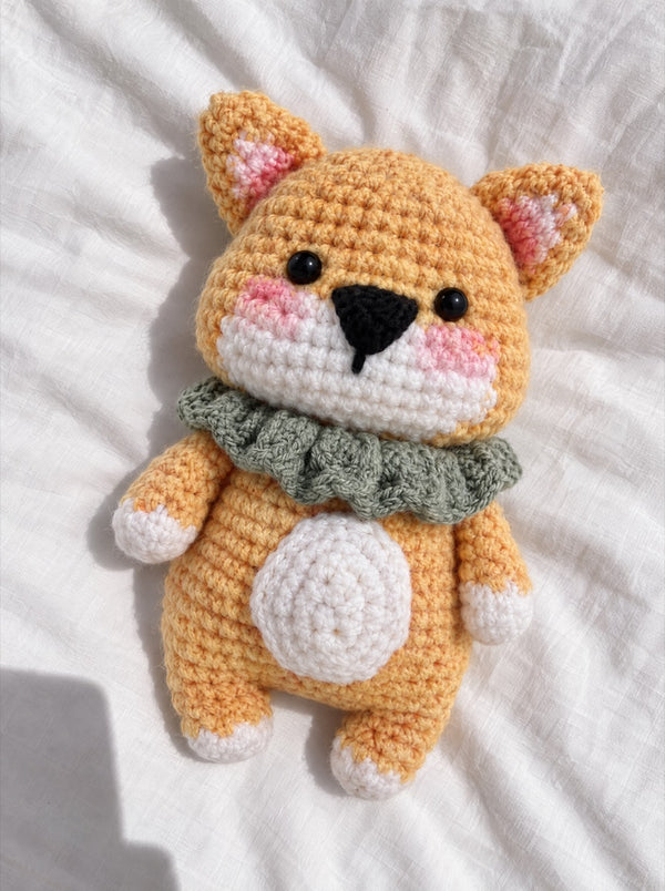 Gehäkelter Shiba mit grünem Kragen auf einem weißen Laken